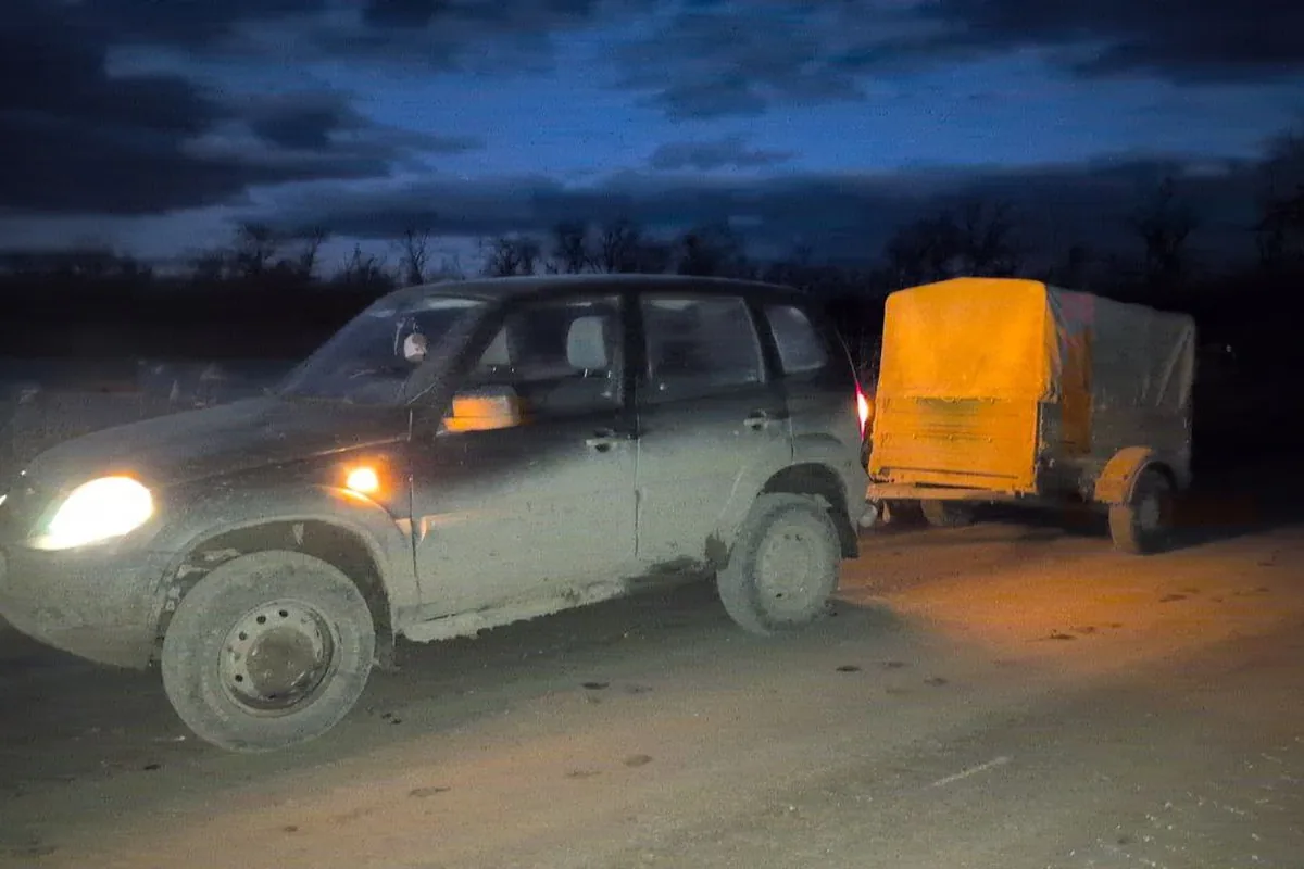 Шевроле Нива с гружёным прицепом вечером на грунтовке