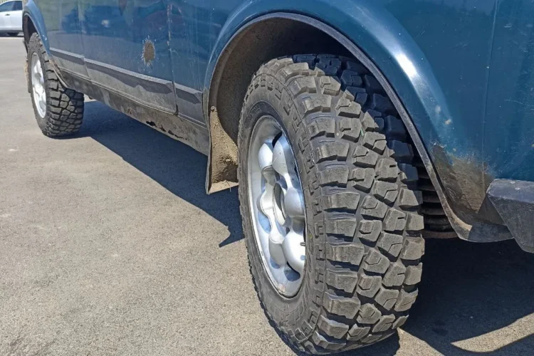 Пятидверная Нива с грязевыми шинами 205/70 R15 на литых дисках, переднее колесо в арке