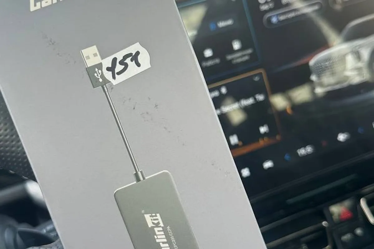 Адаптер Carlinkit в руке на фоне экрана GAC GS8