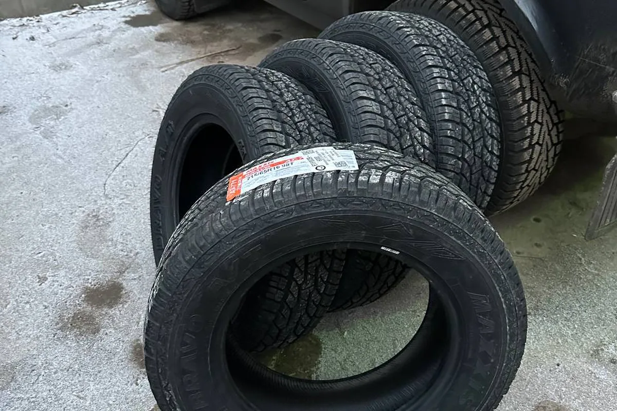 Четыре новые шины 215/65 R16 без шипов у борта чёрной Нивы