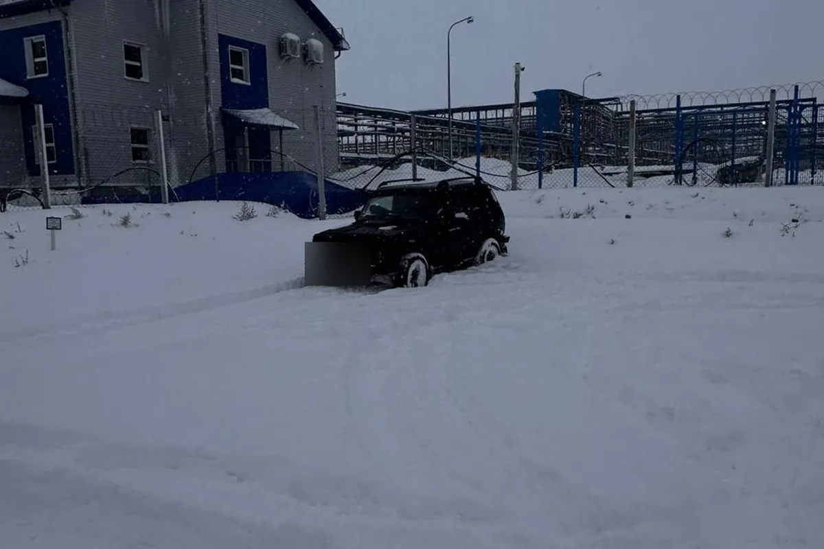 Чёрная Нива в глубоком снегу у промышленного объекта