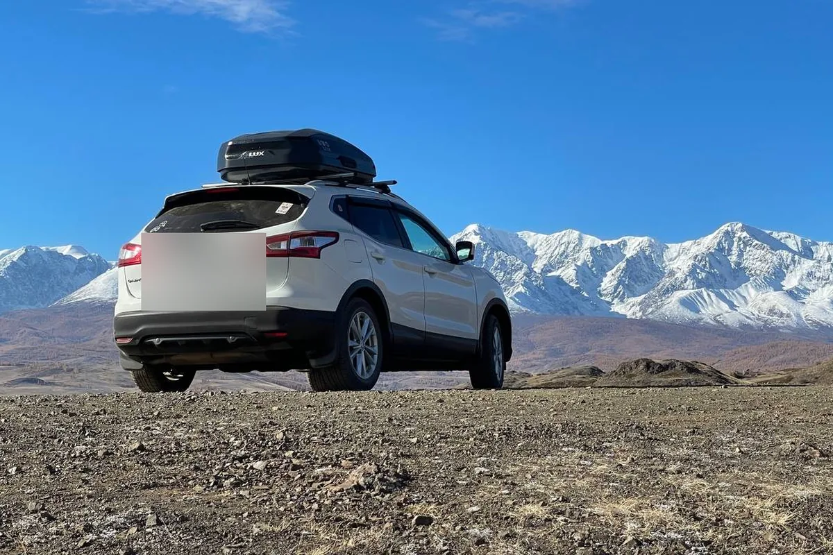 Белый Nissan Qashqai J11 с автобоксом на крыше на фоне гор