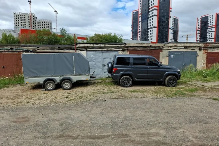 Чёрный УАЗ Патриот с тентованным прицепом у гаражей