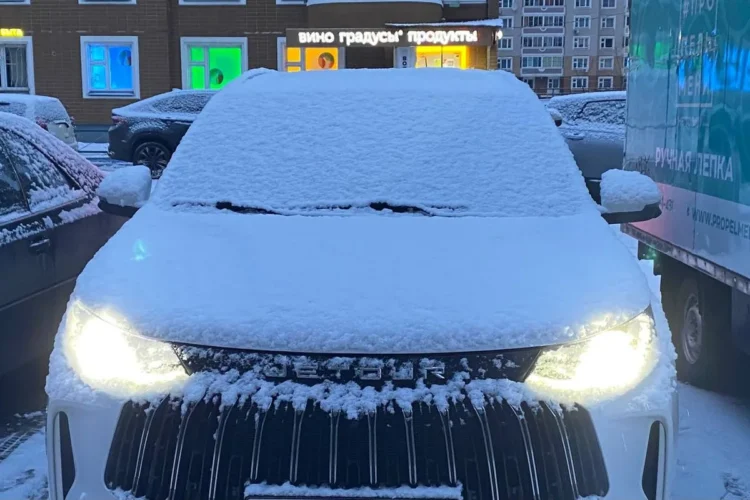 Заснеженный Jetour X70 Plus с включёнными фарами во дворе
