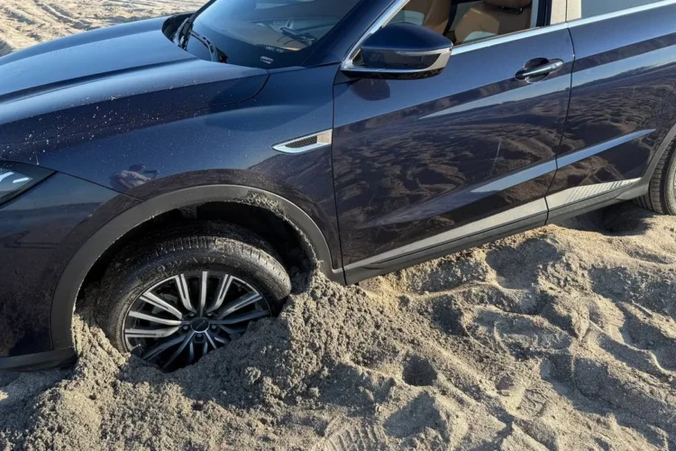 Jetour X70 Plus в песке, вид сбоку на застрявшее колесо