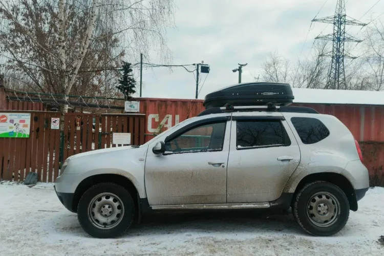 Серебристый Renault Duster с боксом на крыше зимой